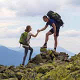 Woman helping unstable male teammate down some rocks while hiking